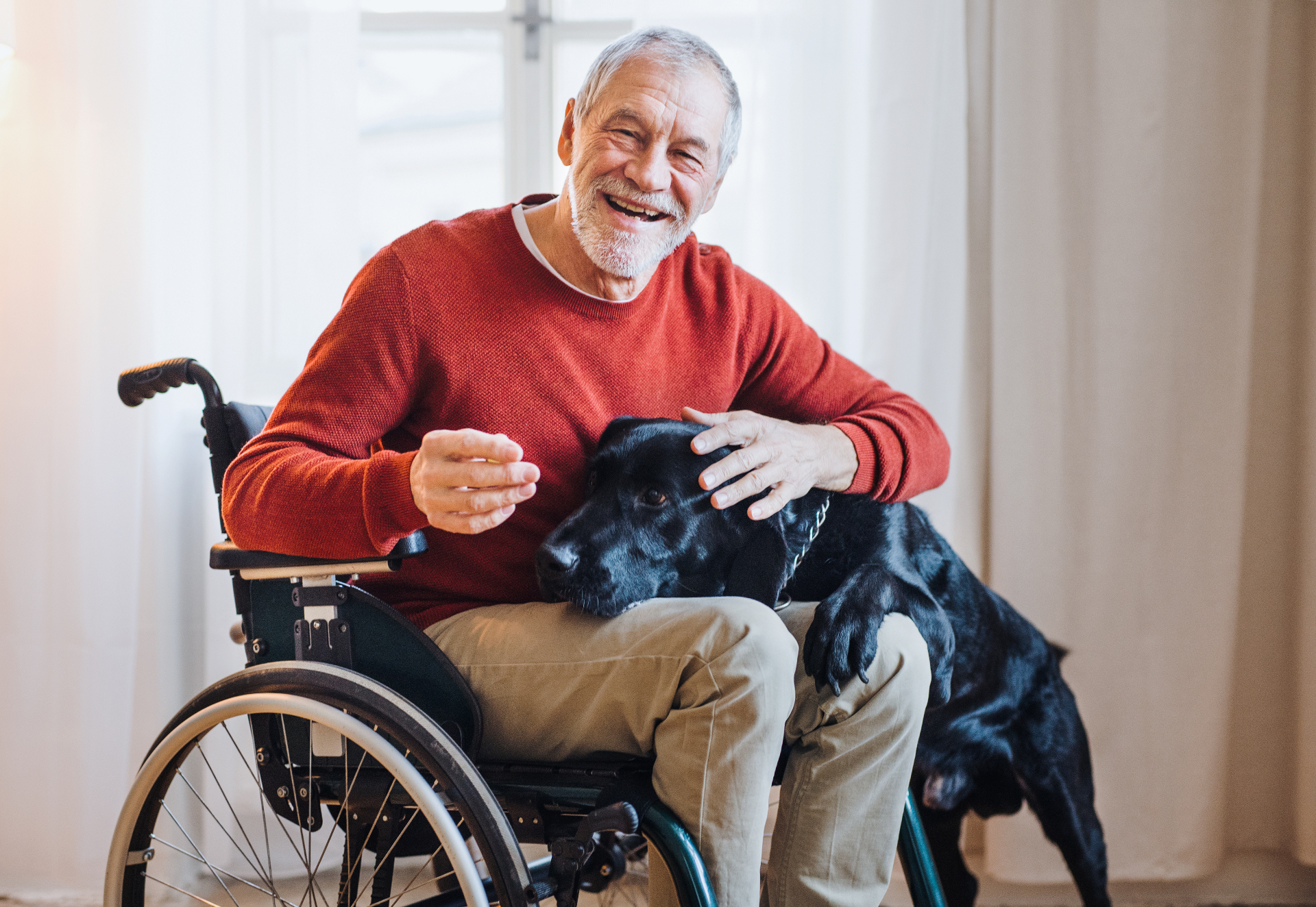 Lachende oudere man in een rolstoel met zijn hond thuis